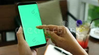 4K镜头。 在咖啡店用绿色屏幕关闭女士手拿智能手机，在手机屏幕上使用手指触摸。